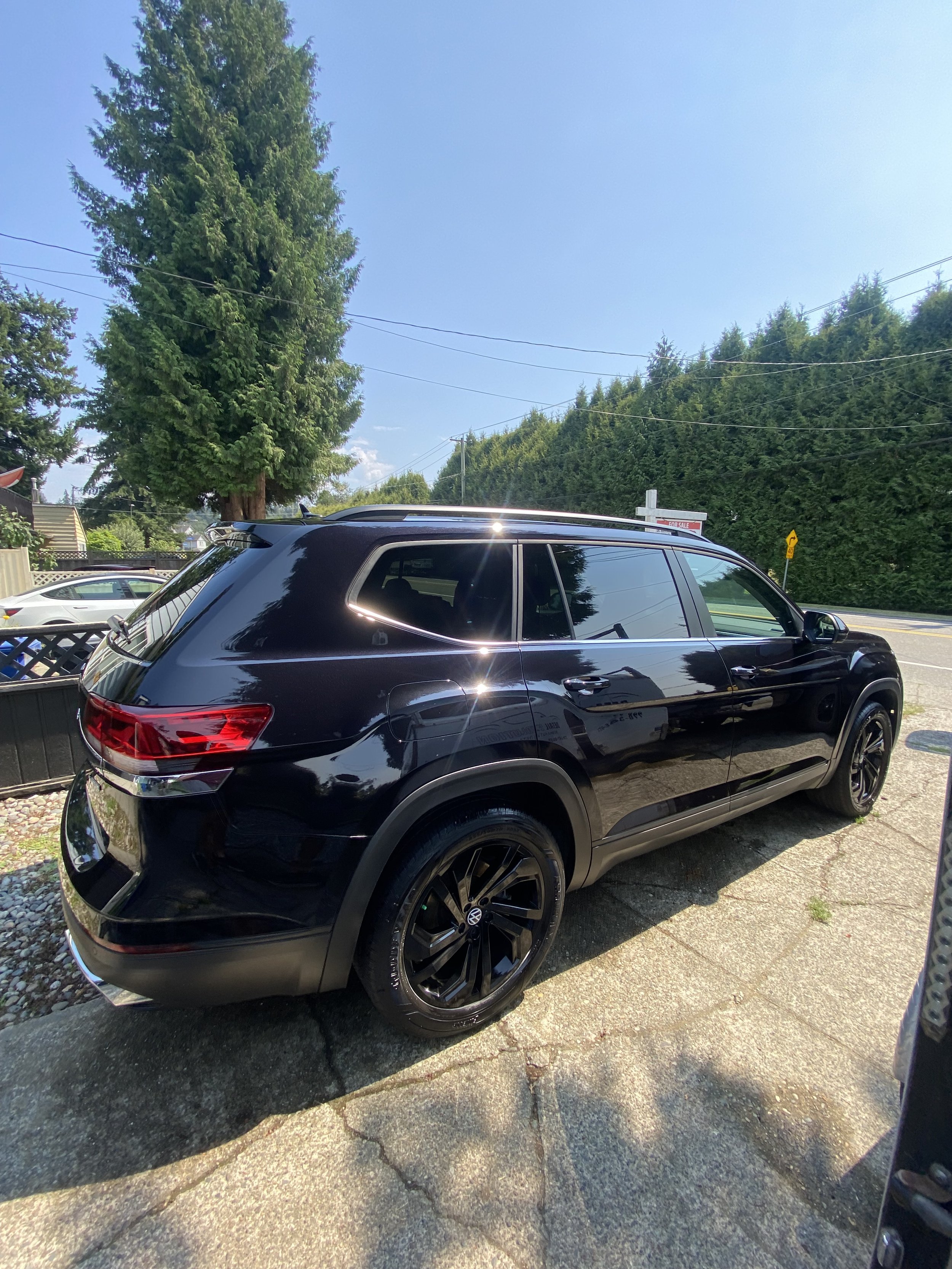 Black SUV parked on a driveway on a sunny day with trees and power lines in the background.