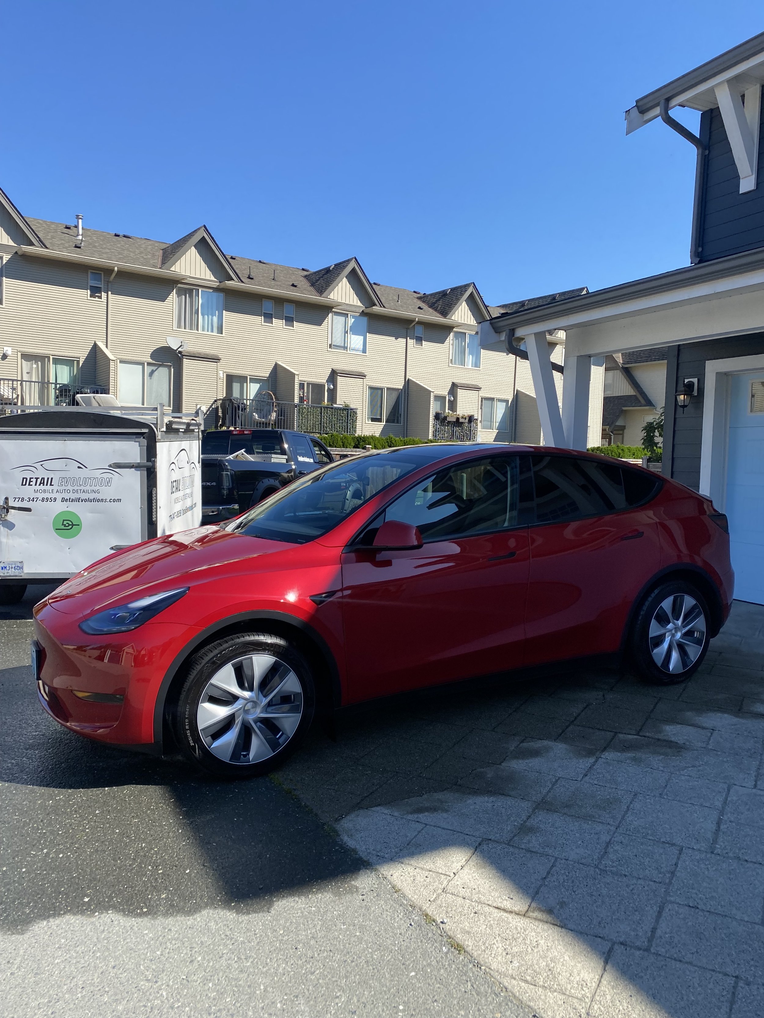 Red Tesla Model 3 parked in driveway of a residential area.
