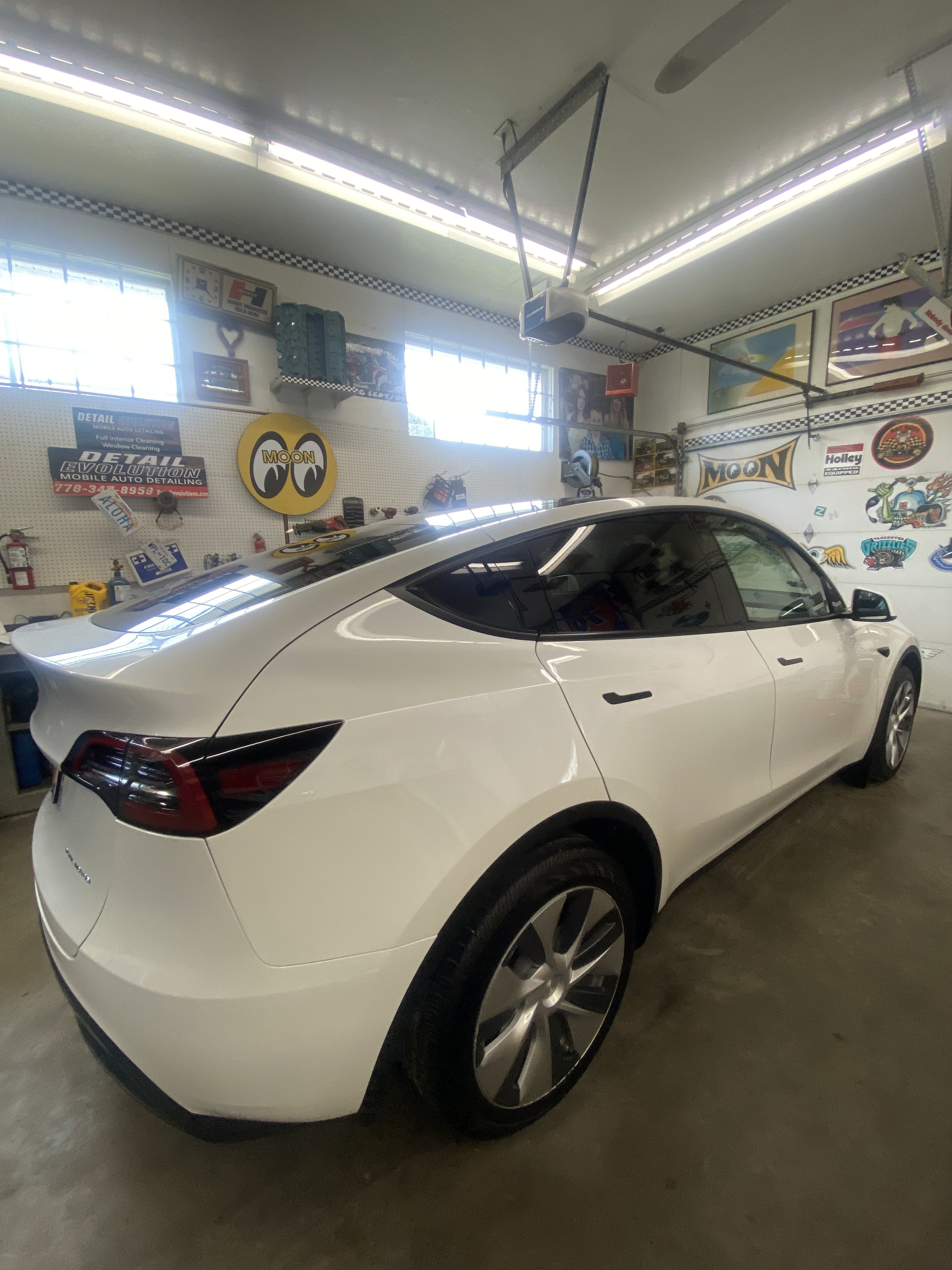 White electric car parked in a garage with various automotive posters and decorations on the walls.